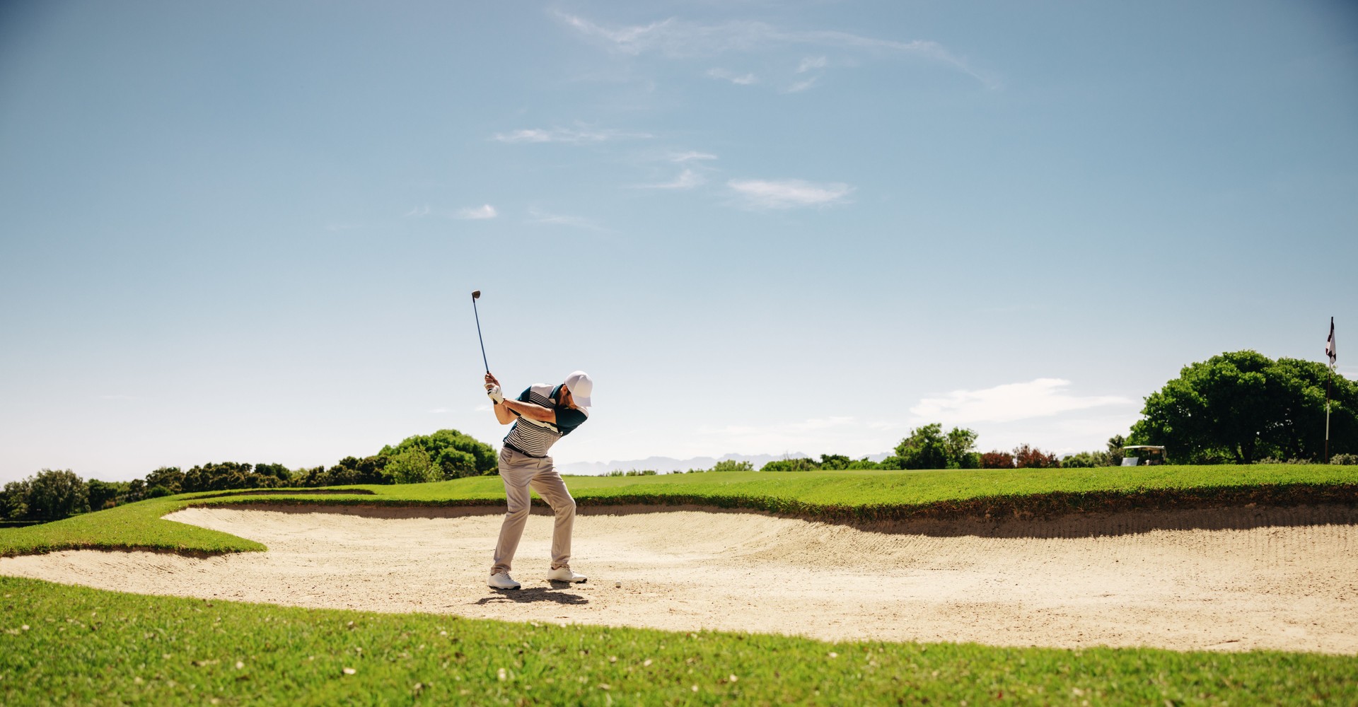 Male golfer swinging golf club in bunker escape during match